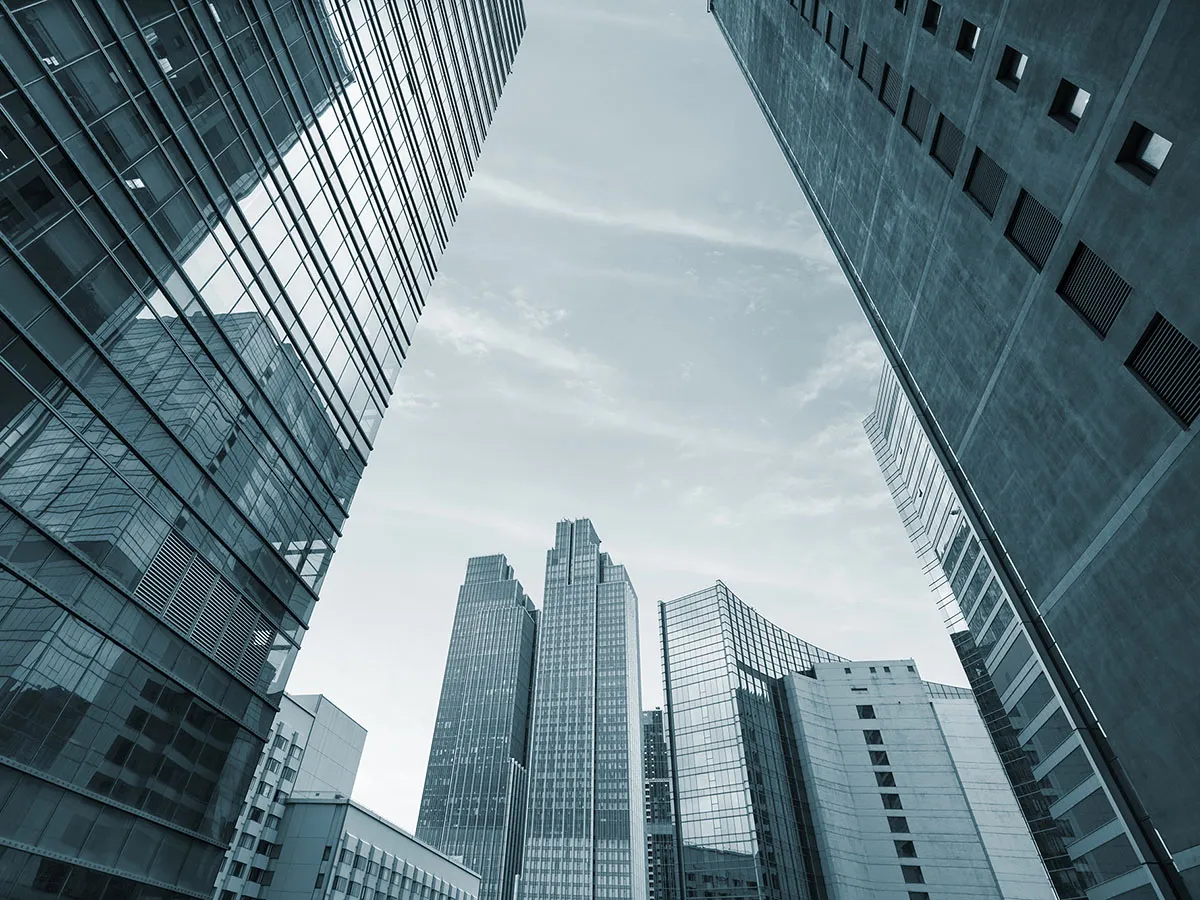 A low-angle view of modern skyscrapers with glass facades against a partly cloudy sky, creating an urban and architectural scene.