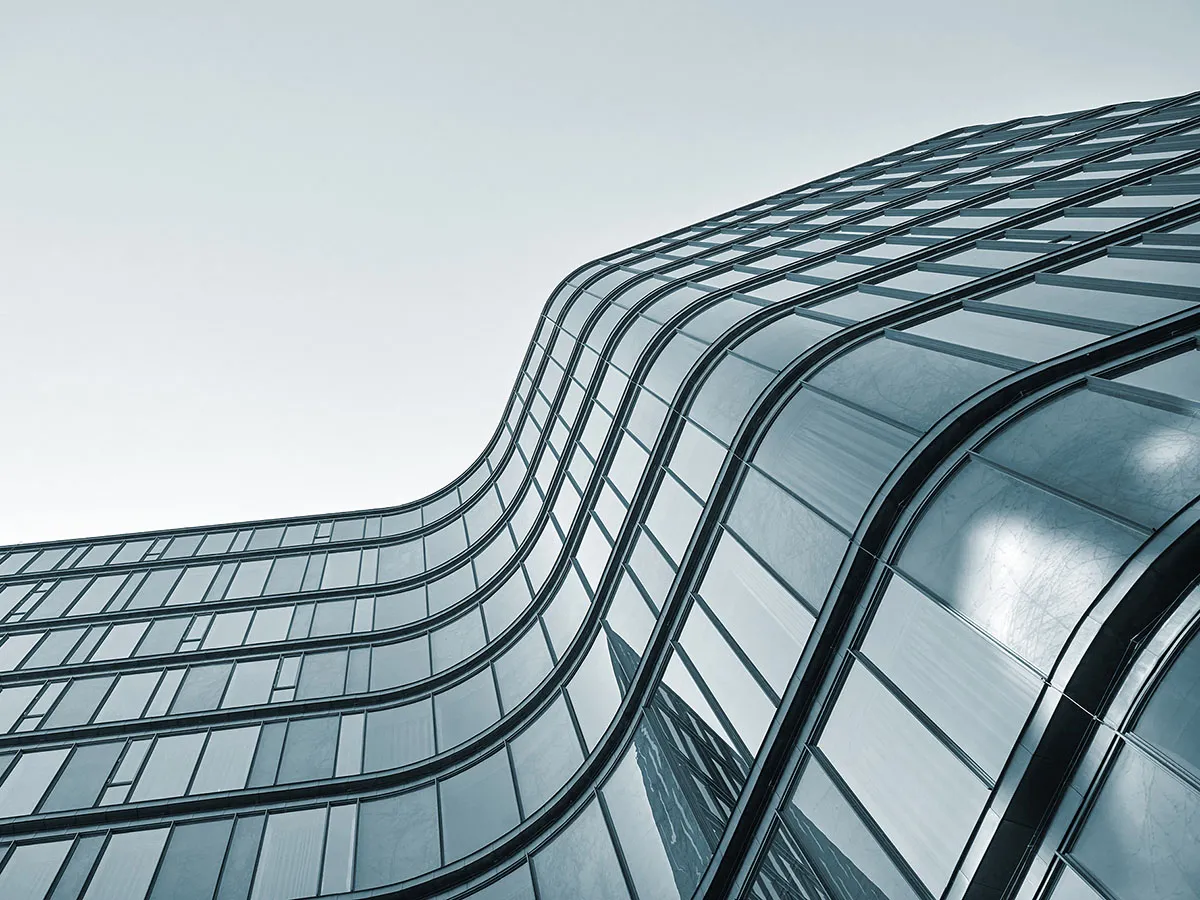 Modern building with curving glass facade and reflective windows against a clear sky background.
